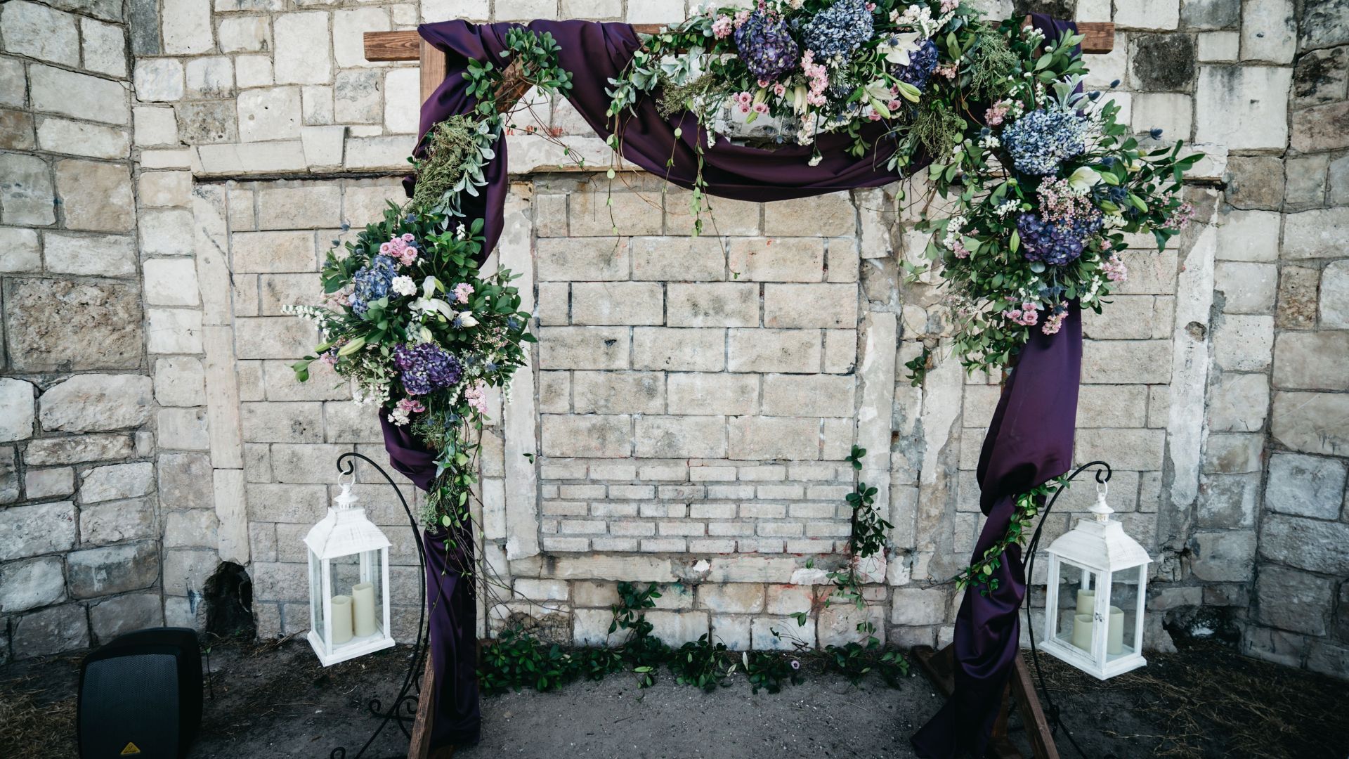 eggplant purple and wooden wedding arch with rock wall backdrop